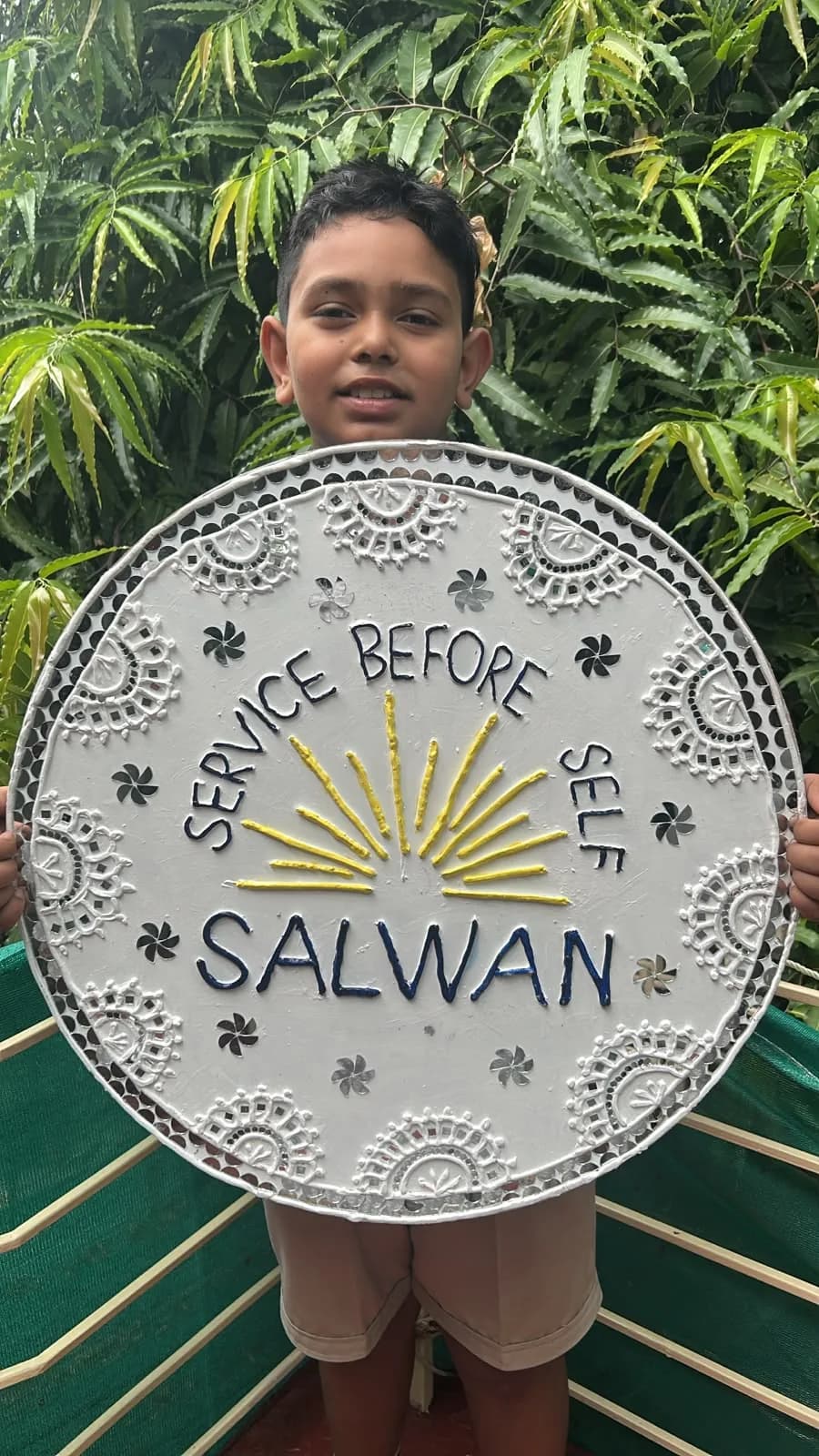 A Salwan Junior School student holding a handcrafted 'Service Before Self, Salwan' emblem